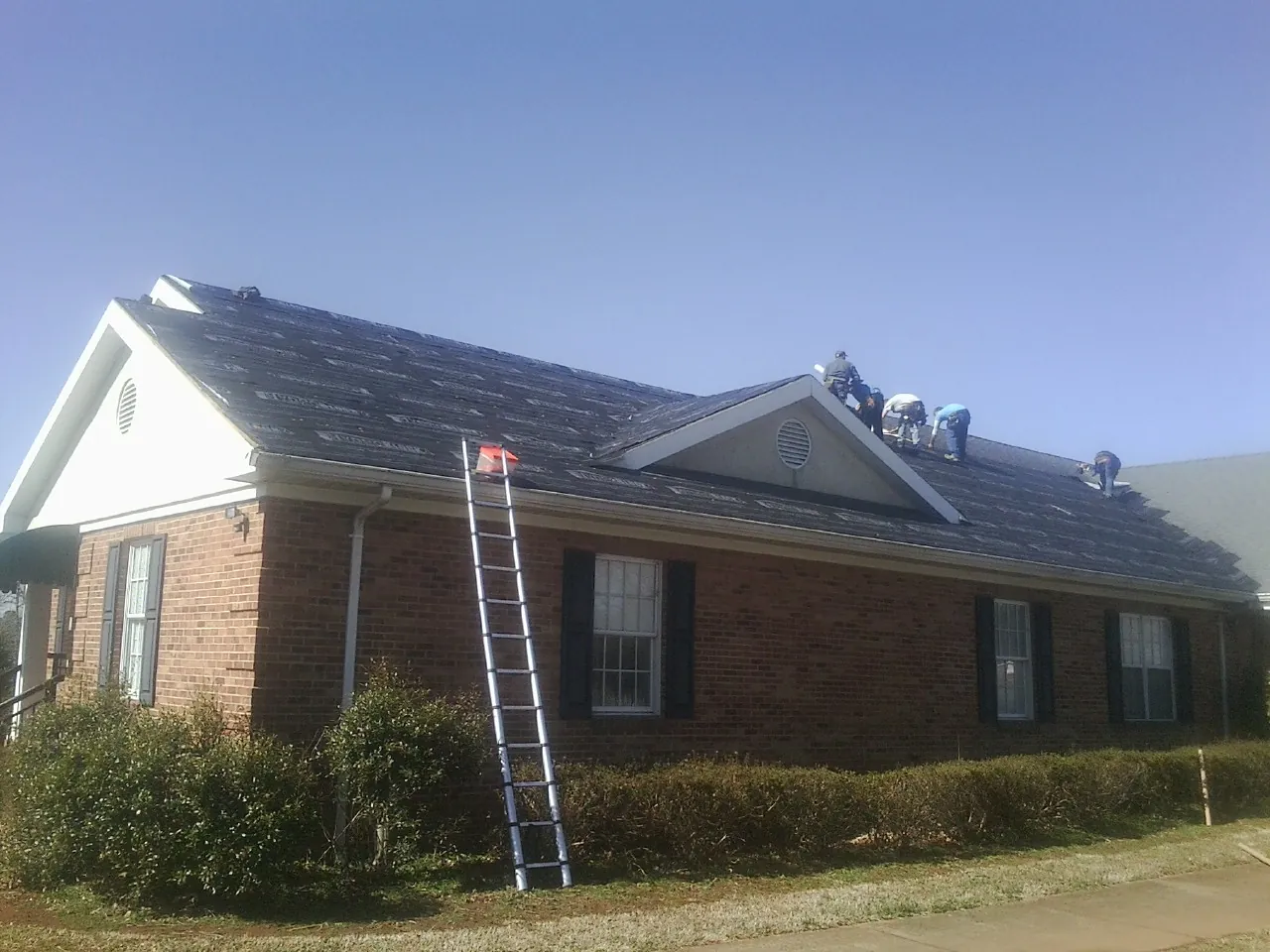 Crew tearing shingles off a brick ranch roof with a ladder set — Emergency Roof Repair work by our crew in Mount Hope