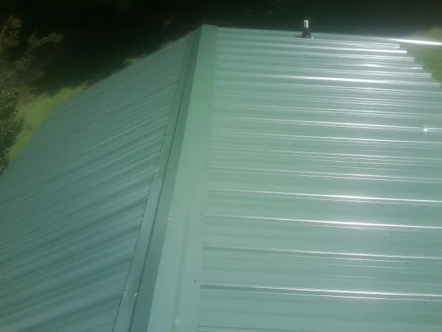 New green metal panels meeting at the ridge of a roof — Flat Roof Repair work by our crew in Mount Hope