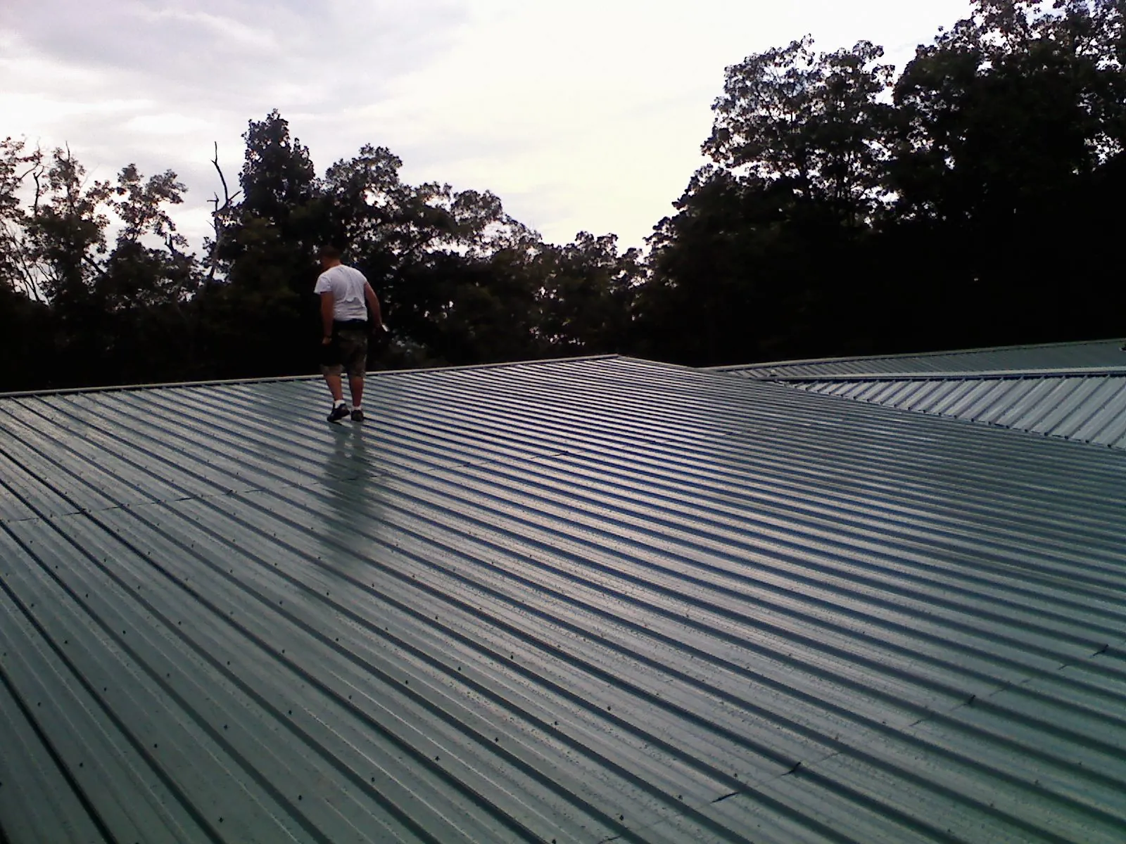 Roofer walking a wide expanse of new green metal roofing in Mount Hope