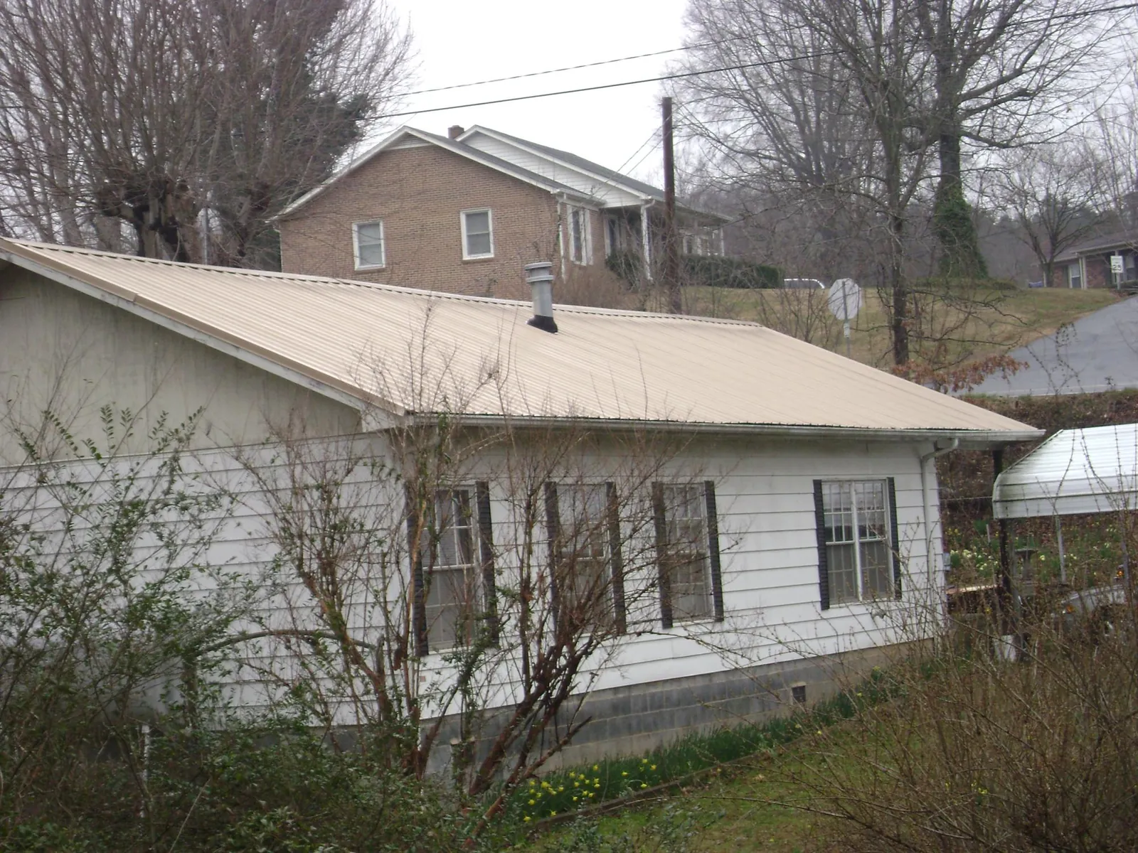 Tan metal roof on a white sided house set into a hillside — Commercial Roofing by Roofing Brothers in Mount Hope
